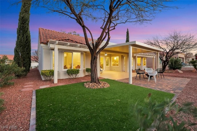 back of property featuring stucco siding, a lawn, a tile roof, and a patio area