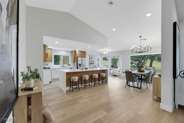 kitchen featuring a breakfast bar, a sink, a kitchen island, stainless steel fridge with ice dispenser, and light countertops