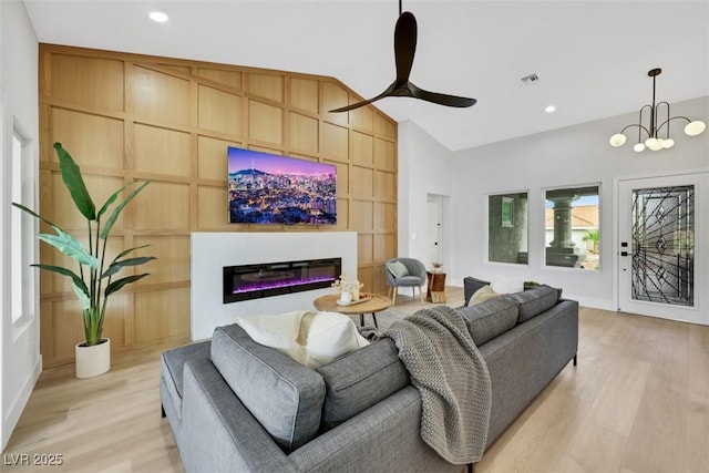 living area with visible vents, built in features, light wood-type flooring, vaulted ceiling, and a glass covered fireplace