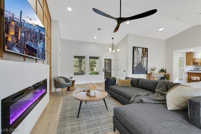 living room featuring visible vents, lofted ceiling, light wood-style flooring, recessed lighting, and a glass covered fireplace