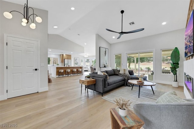 living area featuring visible vents, high vaulted ceiling, a glass covered fireplace, recessed lighting, and light wood-style floors