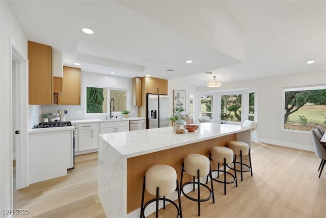 kitchen featuring a kitchen bar, light wood-type flooring, a sink, a center island, and stainless steel appliances