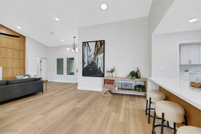 living area featuring baseboards, light wood-style flooring, recessed lighting, vaulted ceiling, and a notable chandelier