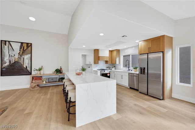 kitchen featuring a sink, light wood-type flooring, appliances with stainless steel finishes, and a breakfast bar