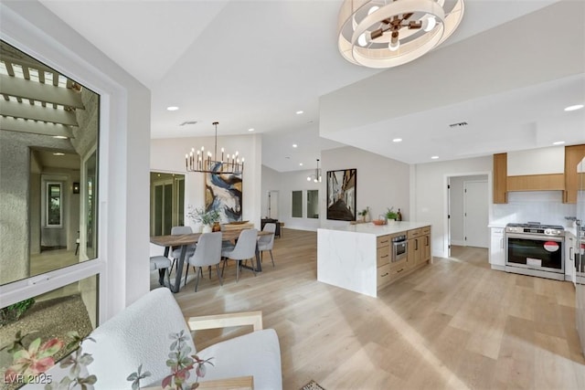 kitchen with lofted ceiling, a notable chandelier, light wood finished floors, and stainless steel gas range oven