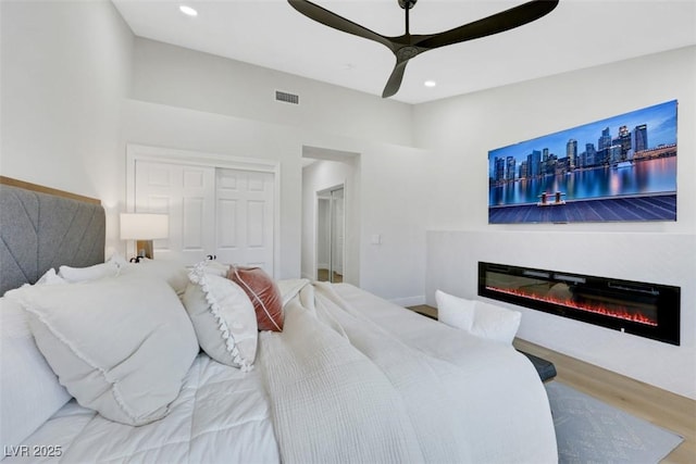 bedroom with recessed lighting, visible vents, wood finished floors, and a glass covered fireplace