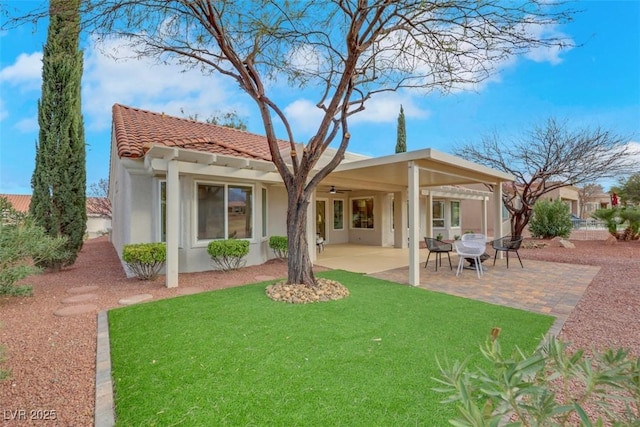 rear view of house featuring a tiled roof, stucco siding, a lawn, a patio, and a ceiling fan