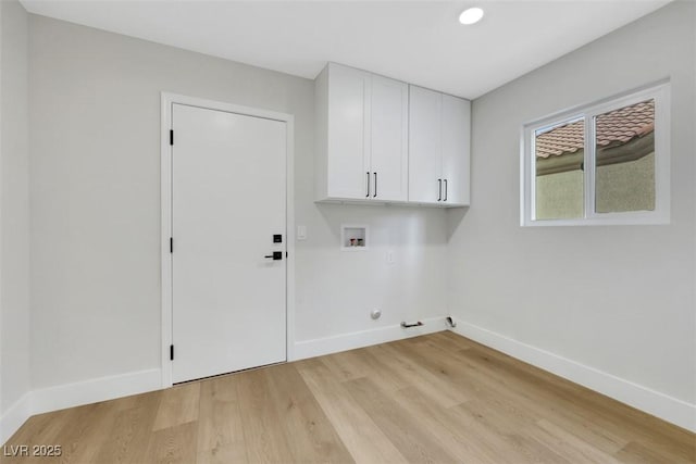 clothes washing area featuring cabinet space, baseboards, and light wood finished floors