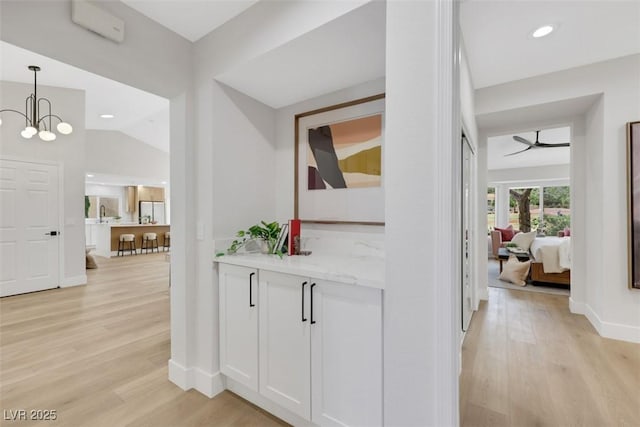 corridor featuring baseboards, light wood-type flooring, vaulted ceiling, recessed lighting, and an inviting chandelier