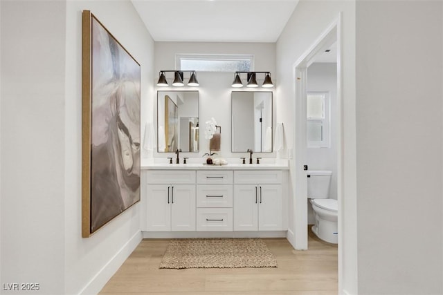 bathroom with double vanity, toilet, wood finished floors, and a sink