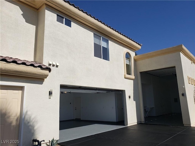 exterior space featuring a tile roof, a garage, and stucco siding