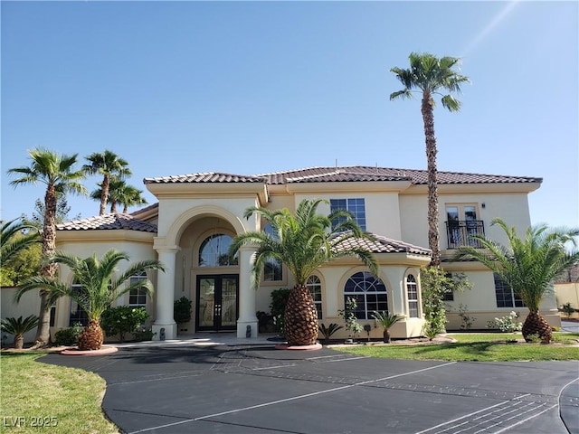 view of front facade featuring a tiled roof, stucco siding, french doors, a balcony, and driveway