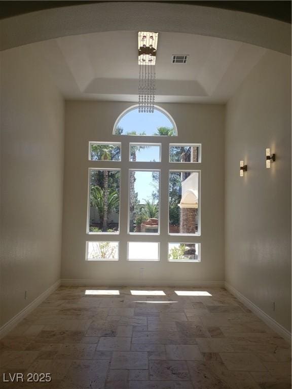 empty room featuring a tray ceiling, a healthy amount of sunlight, visible vents, and arched walkways