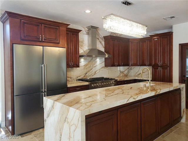 kitchen featuring visible vents, high end fridge, a sink, hanging light fixtures, and wall chimney exhaust hood