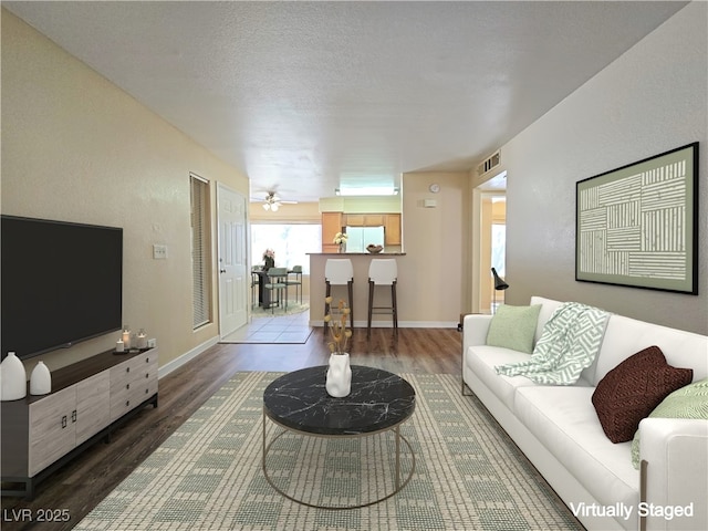 living area with visible vents, a textured ceiling, baseboards, and wood finished floors