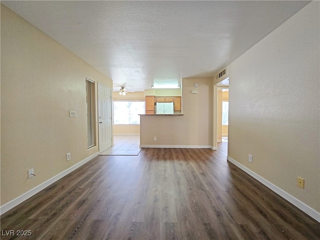 unfurnished living room featuring visible vents, baseboards, a textured ceiling, and dark wood-style floors