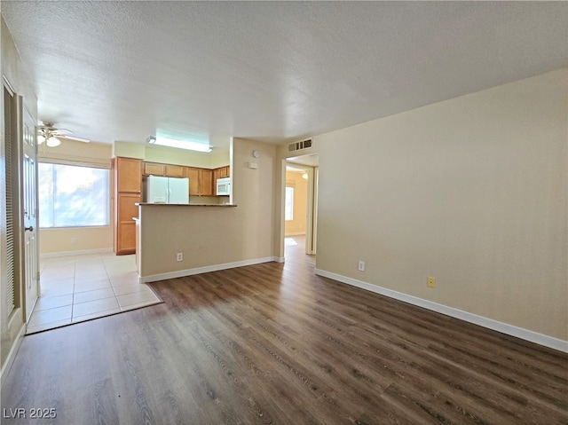 unfurnished living room featuring visible vents, a textured ceiling, baseboards, and wood finished floors