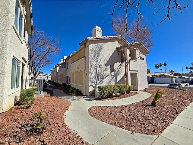 view of property exterior featuring a residential view, stucco siding, a tiled roof, and a chimney