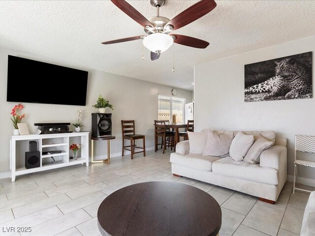 living area featuring tile patterned flooring, ceiling fan, baseboards, and a textured ceiling