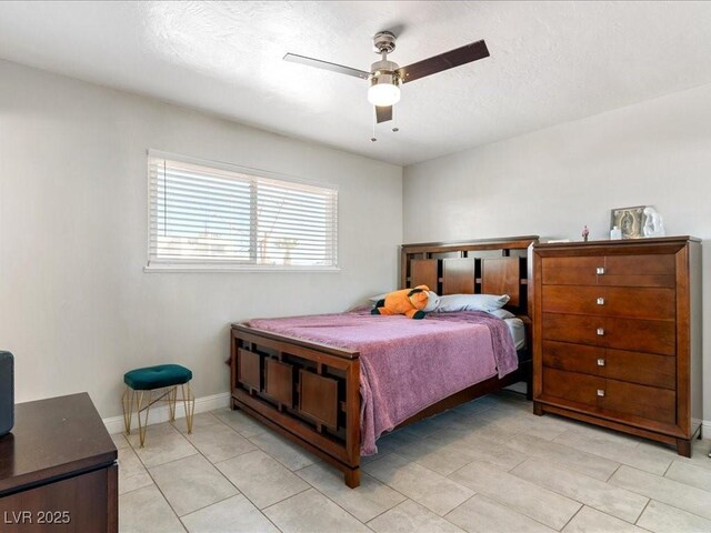 bedroom with a textured ceiling, light tile patterned floors, baseboards, and ceiling fan