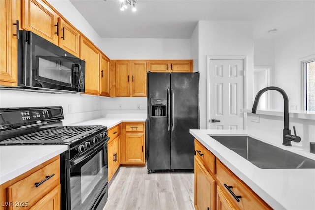 kitchen featuring black appliances, light countertops, light wood-style floors, and a sink