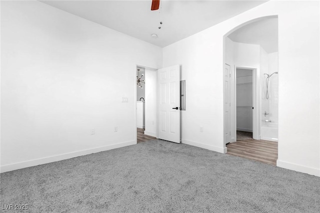 unfurnished bedroom featuring a ceiling fan, baseboards, carpet floors, arched walkways, and a spacious closet