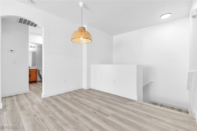 unfurnished room with baseboards, visible vents, arched walkways, and light wood-type flooring