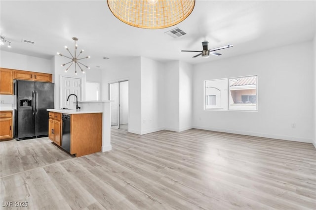 kitchen with brown cabinetry, open floor plan, black appliances, and a sink