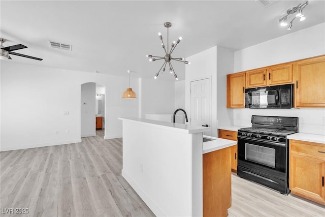 kitchen featuring a kitchen island with sink, arched walkways, black appliances, light countertops, and ceiling fan with notable chandelier