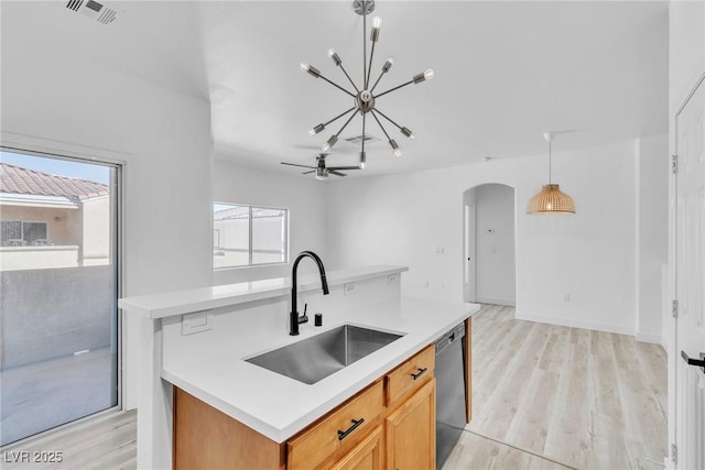 kitchen featuring a sink, arched walkways, light wood-style floors, light countertops, and dishwashing machine