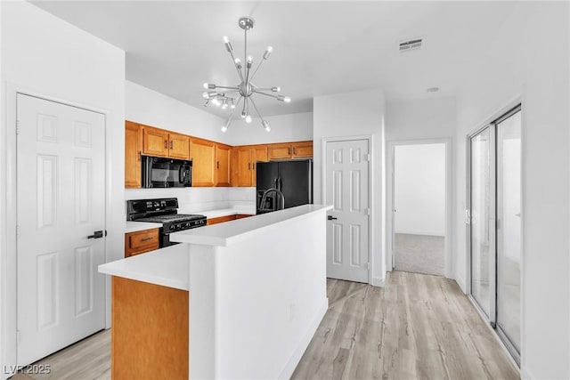 kitchen featuring visible vents, light countertops, light wood-type flooring, an inviting chandelier, and black appliances