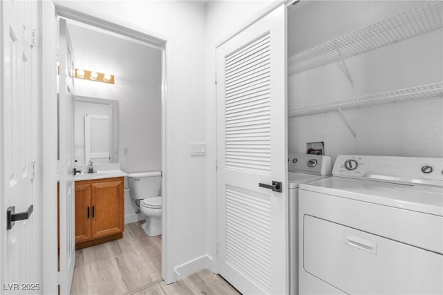 laundry area featuring light wood finished floors, baseboards, washer and clothes dryer, laundry area, and a sink