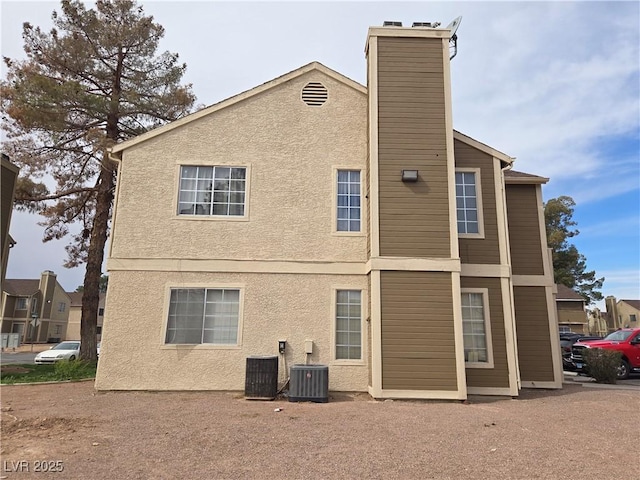 back of property featuring central air condition unit, a chimney, and stucco siding