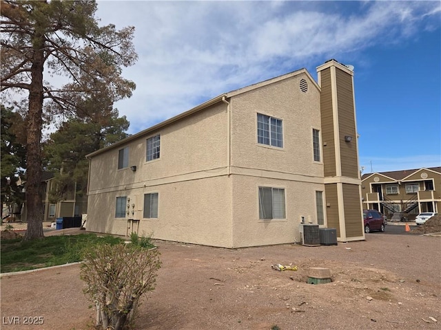 view of property exterior with stucco siding, cooling unit, and a chimney