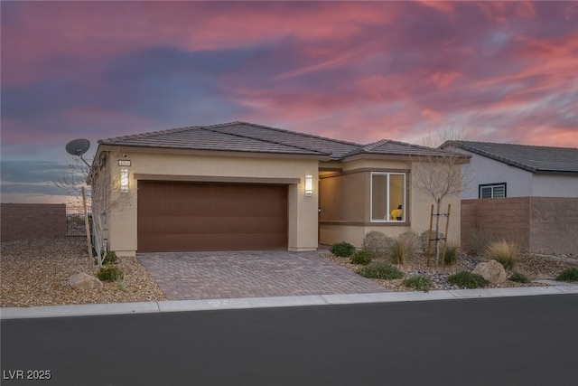 view of front of property featuring stucco siding, decorative driveway, a garage, and fence