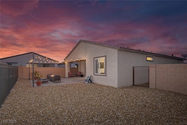 back of property at dusk featuring a patio, a fenced backyard, and stucco siding