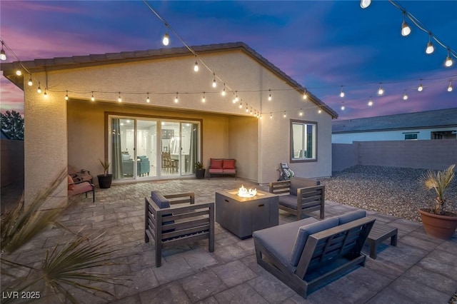 patio terrace at dusk featuring an outdoor living space with a fire pit and fence