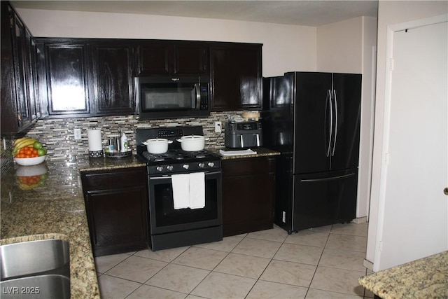 kitchen featuring light tile patterned flooring, stone countertops, decorative backsplash, black appliances, and dark cabinets