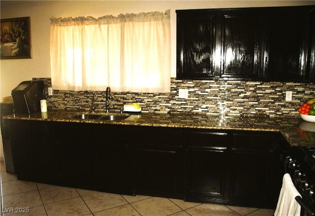 kitchen featuring a sink, dark stone counters, backsplash, and dark cabinetry