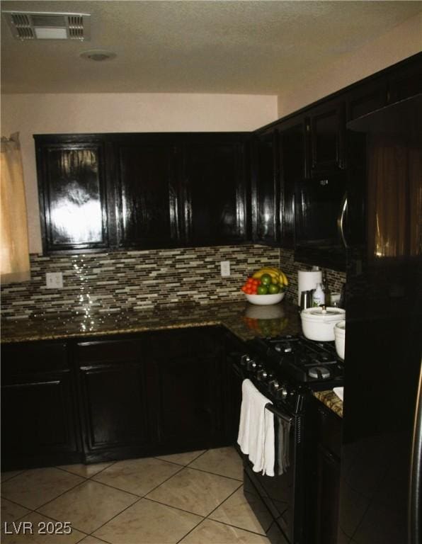 kitchen with dark cabinetry, visible vents, light tile patterned flooring, black appliances, and backsplash