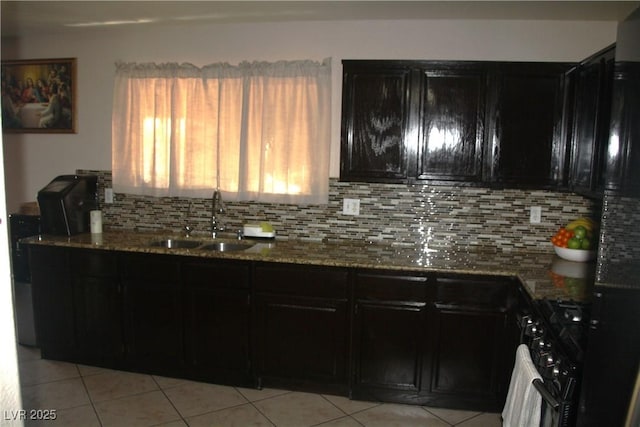 kitchen with backsplash, double oven range, stone counters, dark cabinetry, and a sink