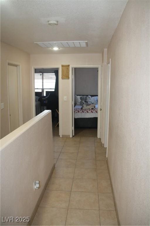 hallway with visible vents, an upstairs landing, and light tile patterned flooring