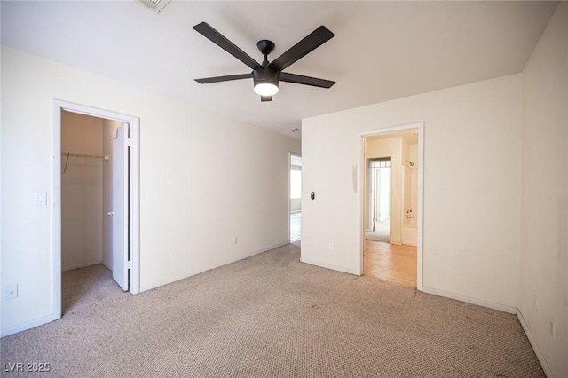 unfurnished bedroom featuring a spacious closet, light colored carpet, a closet, and ceiling fan