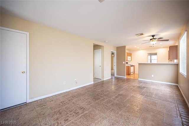 unfurnished living room featuring stone finish flooring, baseboards, visible vents, and ceiling fan