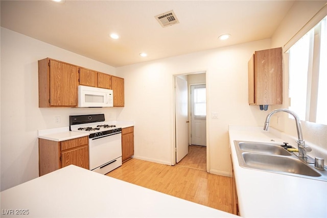 kitchen featuring white appliances, visible vents, light wood-style flooring, a sink, and light countertops