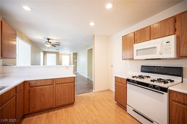 kitchen with light countertops, light wood-type flooring, brown cabinets, a peninsula, and white appliances