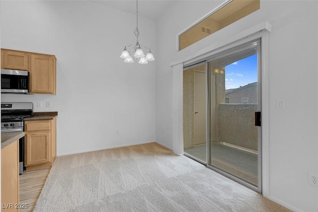 kitchen featuring decorative light fixtures, a chandelier, light carpet, appliances with stainless steel finishes, and a towering ceiling