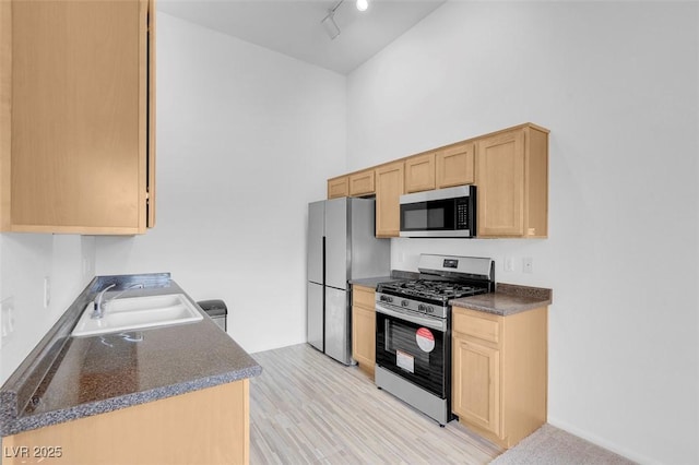 kitchen with dark countertops, light brown cabinets, appliances with stainless steel finishes, and a sink