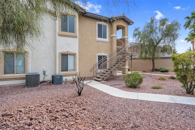 rear view of property with cooling unit, stairway, and stucco siding