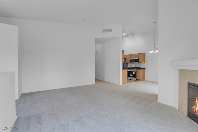 unfurnished living room featuring visible vents, rail lighting, a tiled fireplace, a notable chandelier, and light colored carpet